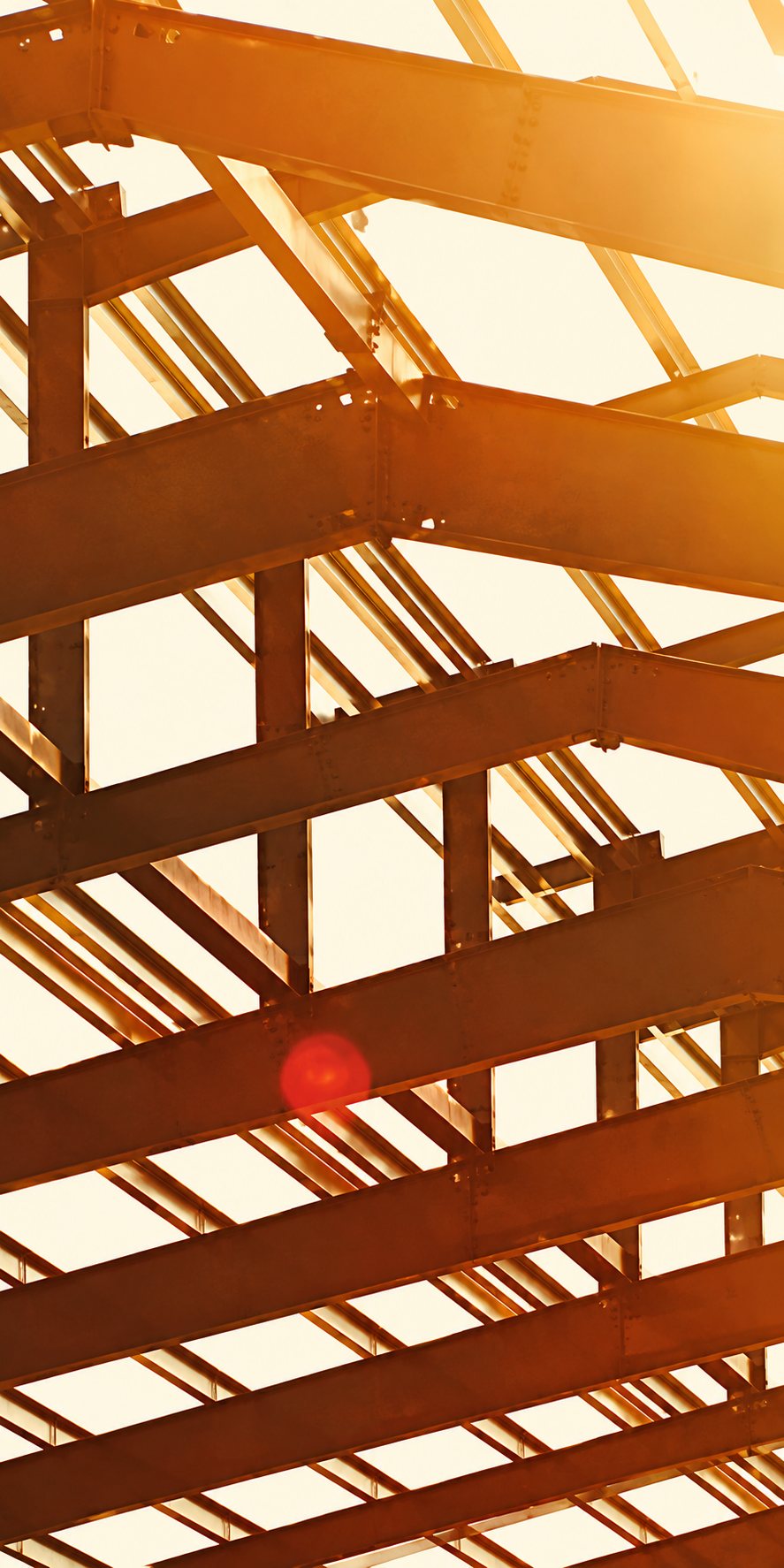 Structure de charpente en bois vue de dessous, éclairée à contre-jour par un soleil orangé.