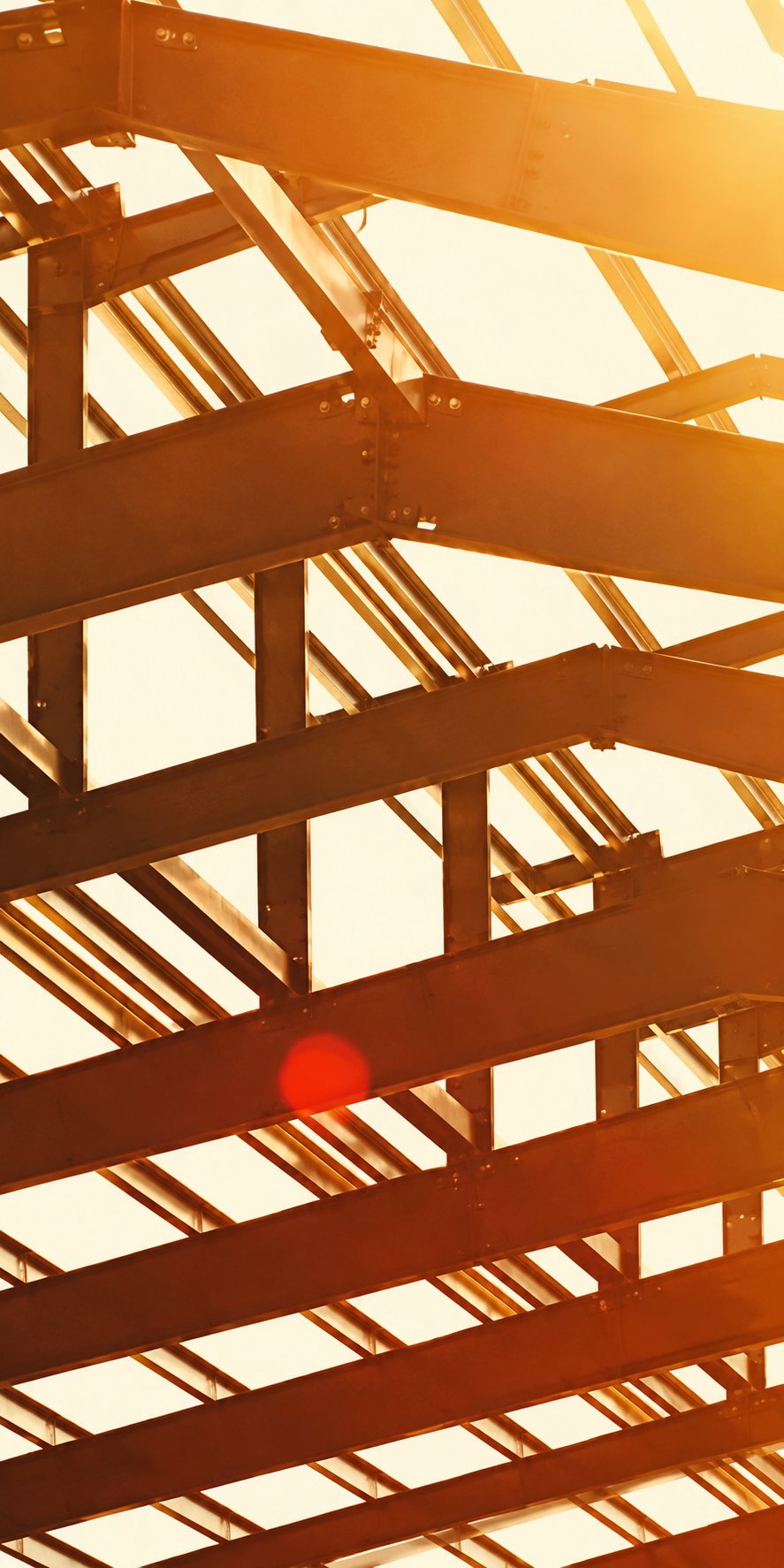 Structure de charpente en bois vue à contre-jour, avec un soleil orangé qui filtre entre les poutres.