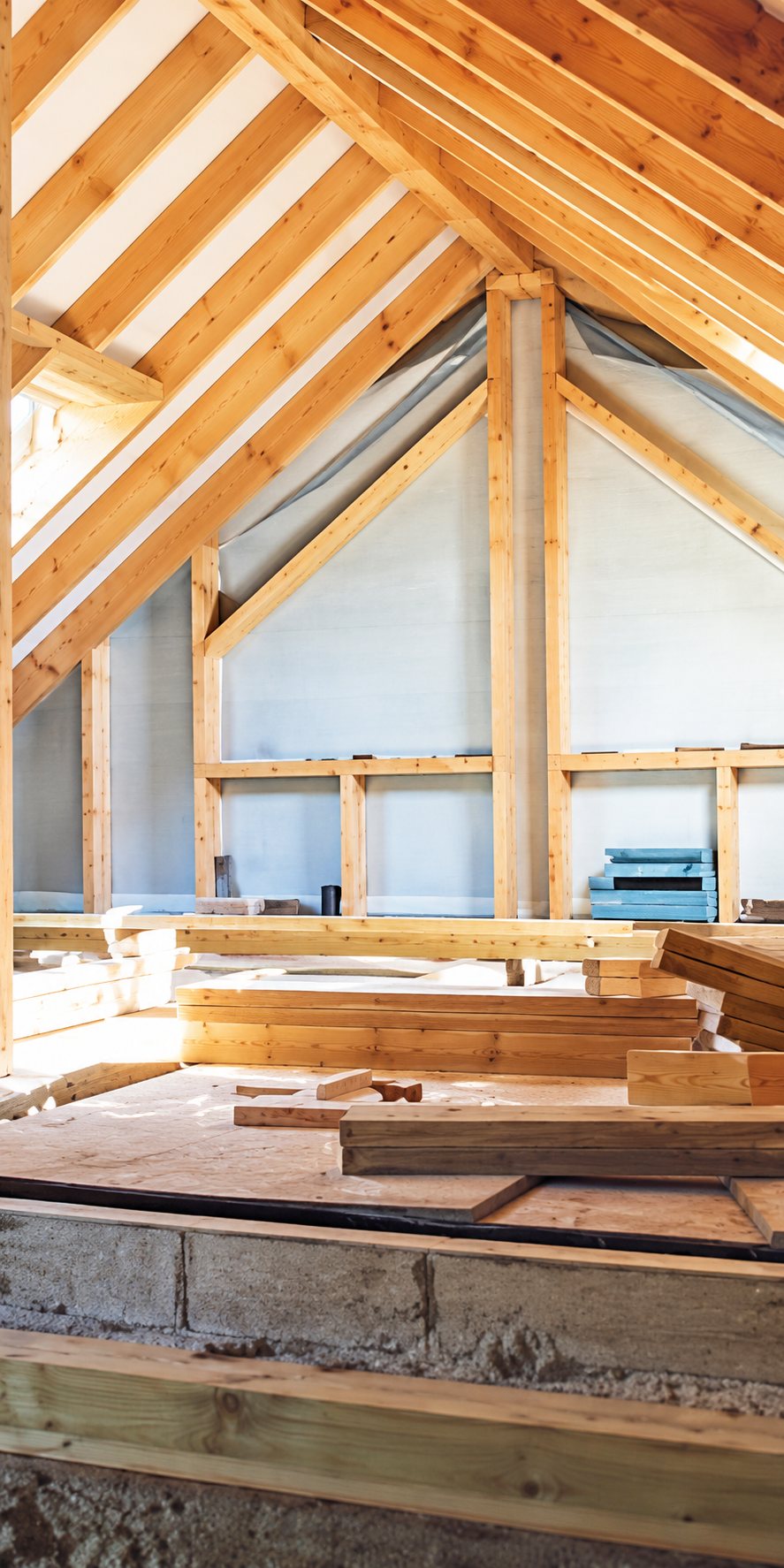 Intérieur d'une maison en chantier dont la charpente en bois clair est apparente, avec des planches empilées au premier plan.