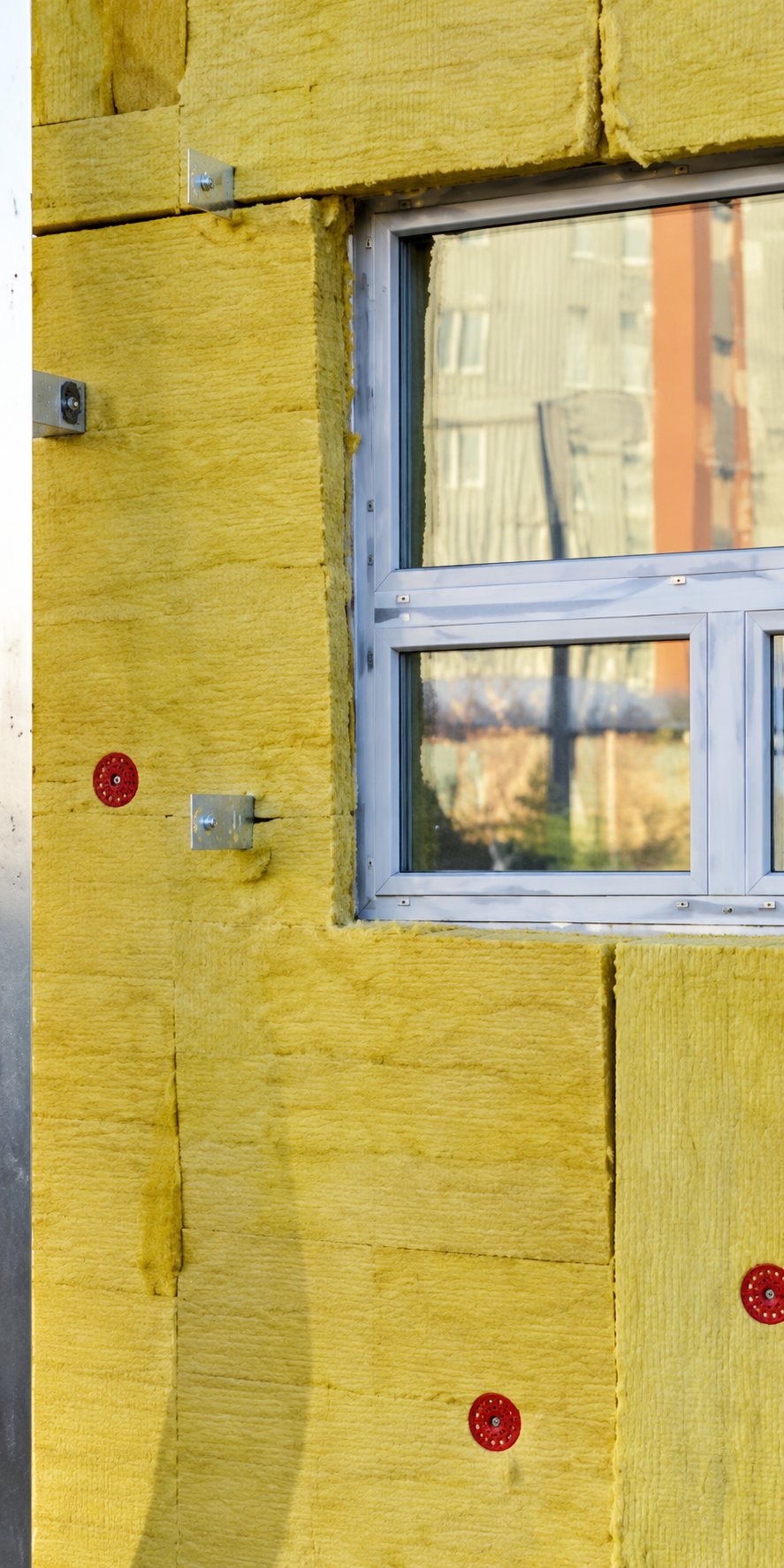 Une fenêtre à cadre blanc est posée dans un mur recouvert de panneaux d'isolation jaunes fixés par des chevilles.