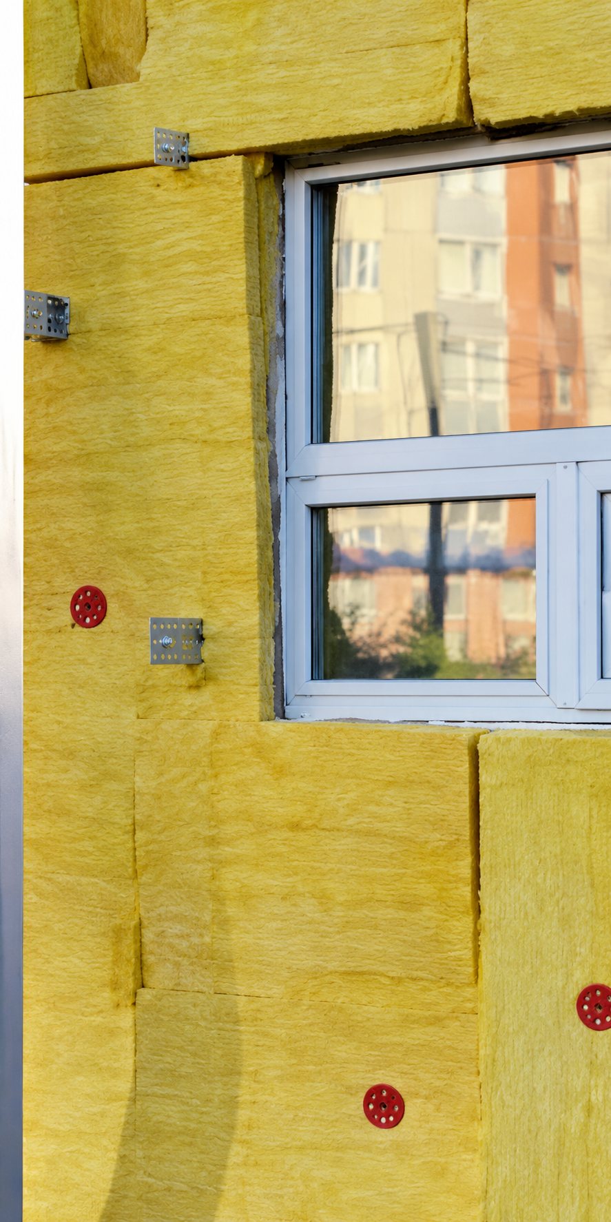 Une fenêtre à cadre blanc est installée dans un mur recouvert de panneaux d'isolation jaunes fixés par des chevilles.