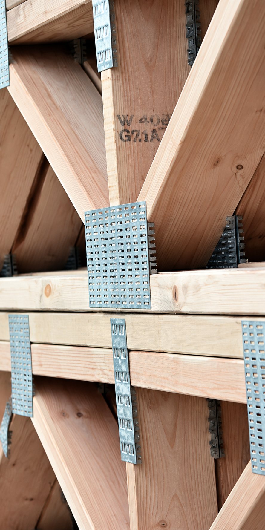 Gros plan sur une charpente en bois dont les poutres sont assemblées par des plaques métalliques perforées.