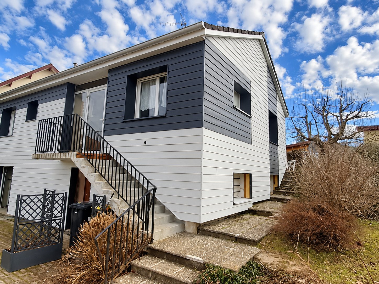 Maison individuelle dont la façade a été rénovée avec un bardage horizontal blanc et gris anthracite, dotée d'un escalier extérieur à rambarde noire.