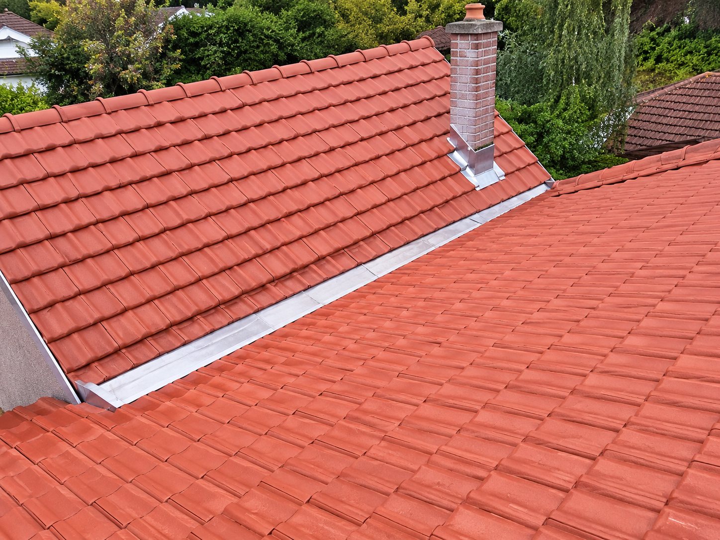 Vue d'une toiture en tuiles rouges avec deux pans et une noue centrale, après travaux de rénovation.