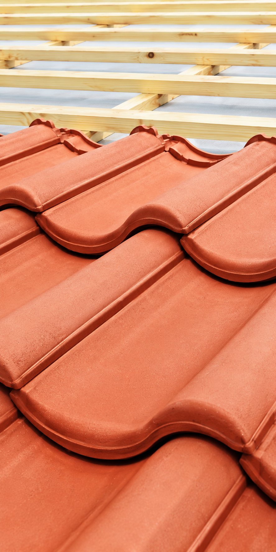 Gros plan sur des tuiles rouges ondulées installées sur une toiture, avec des lattes de bois claires visibles en arrière-plan.